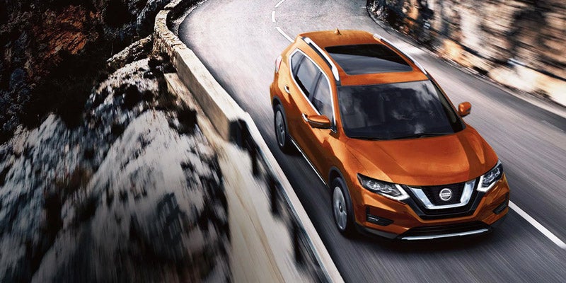 An orange Nissan Rogue driving through the mountain pass