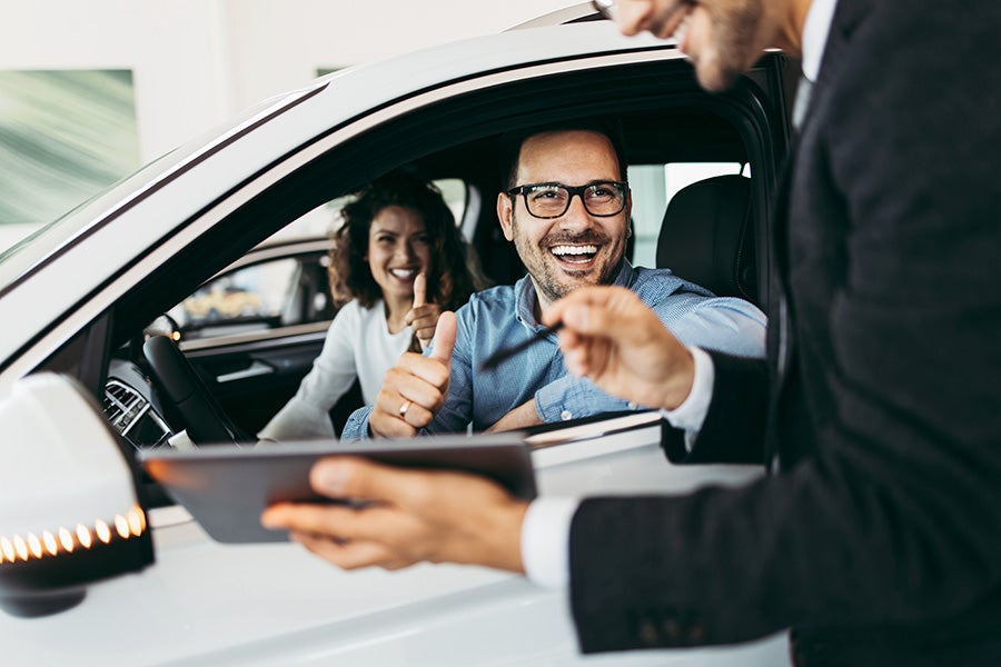 couple in car giving a thumbs up to sales man